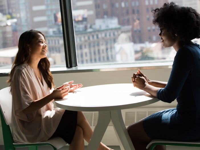 Two women connect for a conversation in an office that overlooks the cityscape.